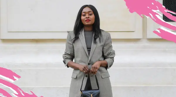 Frau in kariertem Blazer und dunklem Oberteil, perfekt für einen **business casual** Look. Sie trägt eine schwarze Handtasche.