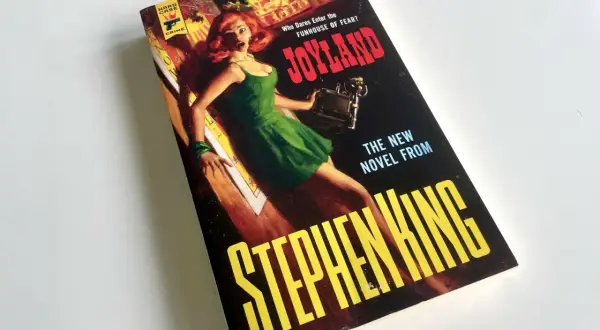Bokomslaget till Stephen Kings "Joyland" med en skräckslagen kvinna i en grön klänning. En av många filmer med Stephen King som väntar på att bli sedd.