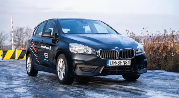 Ciemny BMW 218i na oblodzonej drodze, z logo BMW TEAM Długołęka na drzwiach.