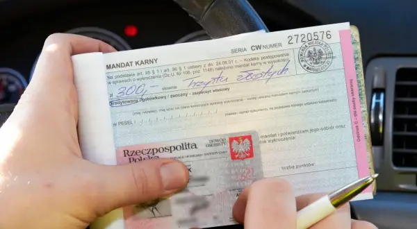 Ręce trzymają mandat karny na 300 zł. Wpisano "trzysta złotych", ale nie widać, ile punktów ma młody kierowca.