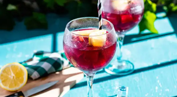 Två glas med tinto de verano, fyllda med is och citronklyftor, står på ett blått bord.