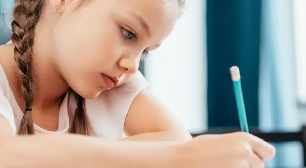 Bambina concentrata scrive con matita. Potrebbe essere una di quei bambini plusdotati 2 anni che già imparano a scrivere.