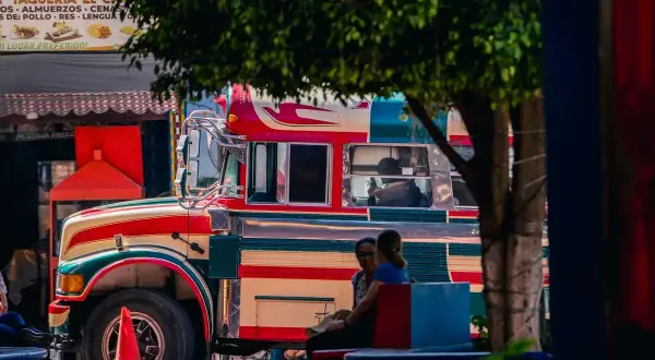 Bunter "chicken bus" in Guatemala, bereit für die nächste Fahrt. Menschen warten auf dem Bürgersteig.