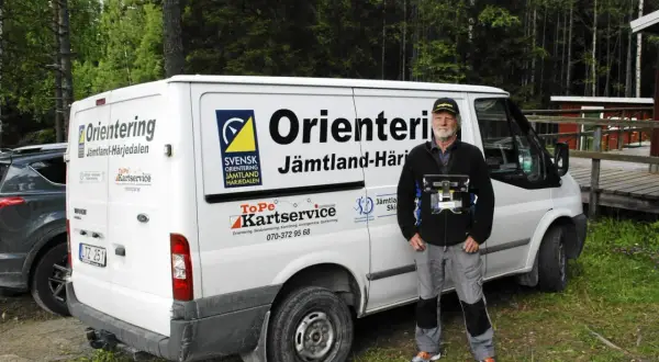 Torgny Pettersson står bredvid en vit skåpbil med texten "Orientering Jämtland-Härjedalen". Han håller i en utrustning för orientering.