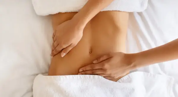 Hände massieren sanft den Bauch einer Frau. Manche empfinden Lymphdrainage als schmerzhaft, doch hier scheint es eine wohltuende Behandlung zu sein.
