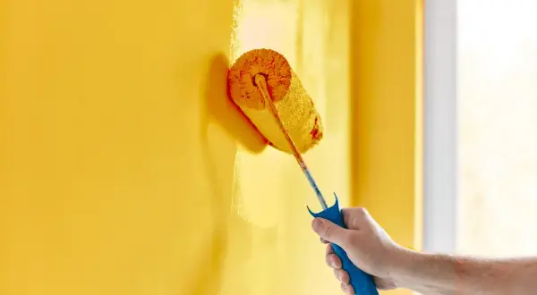 Mano che dipinge un muro di giallo brillante con un rullo. La vernice ha un bellissimo colore opaco che copre uniformemente la superficie.