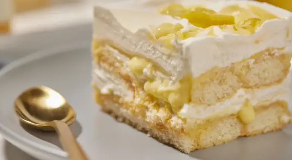 Ein Stück cremiges Lemon Tiramisu mit Löffel auf einem Teller.
