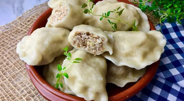 Pyszne pierogi z kaszą gryczaną i twarogiem, udekorowane gałązkami ziół, kuszą swoim domowym wyglądem.
