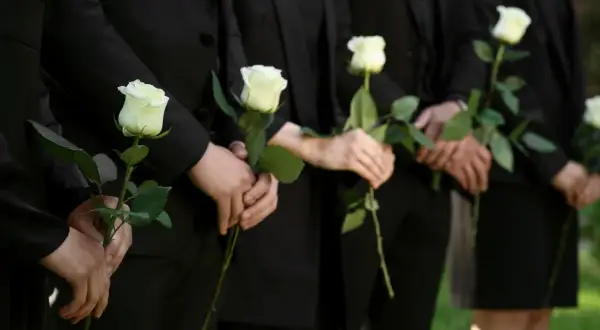 Ludzie w czerni trzymają białe róże. Mogą symbolizować żałobę, ale też nadzieję, która bywa trudna dla osób wierzących, gdy pojawiają się przyczyny lęku przed śmiercią.