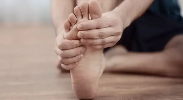 Uomo che si tiene il piede, mostrando i sintomi della metatarsalgia. Dolore sotto l'avampiede.