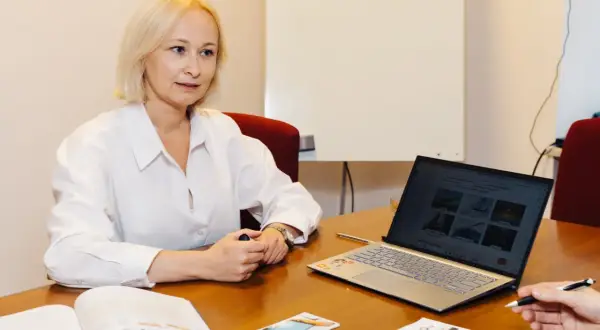 Kobieta w białej koszuli uczy się słówek po rosyjsku, korzystając z laptopa i materiałów drukowanych.