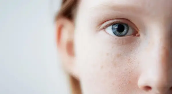 Nahaufnahme eines blauen Auges und der Wange einer Person mit Sommersprossen. Sanfte Pflege für empfindliche Haut ist hier sichtbar.