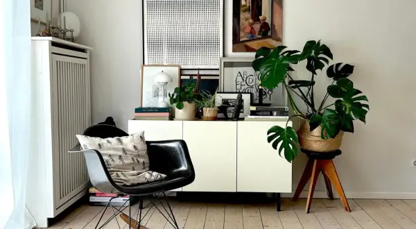 Gemütlich eingerichtetes schmales Reihenhaus: Schwarzer Schaukelstuhl mit Kissen, weißes Sideboard mit Pflanzen und Kunst.