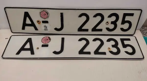 Dwie białe tablice rejestracyjne z czarnymi znakami "AJ 2235". Na górnej tablicy widoczna naklejka z numerem "11" w okręgu. To typowe niemieckie tablice rejestracyjne.