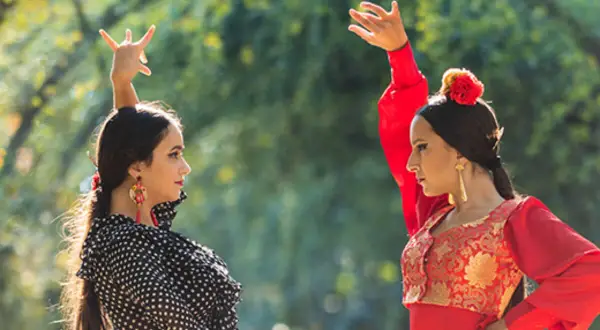 Dos bailarinas de un grupo flamenco famoso, con trajes vibrantes, ejecutan pasos elegantes bajo la luz del sol.