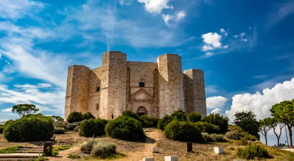 Castel del Monte, un'imponente fortezza ottagonale, si erge su una collina sotto un cielo azzurro e nuvoloso. Un luogo perfetto per chi ama visitare Castel del Monte.
