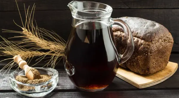 Dzbanek z ciemnym napojem, bochenek chleba, kłosy zboża i miseczka z mąką. Czy podpiwek ma alkohol? To pytanie nurtuje wielu.