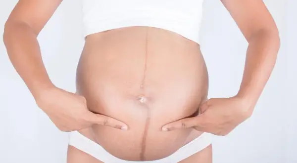 Kreska na brzuchu w ciąży, symbol przemiany. Dwie dłonie wskazują na ciemną linię biegnącą przez środek.