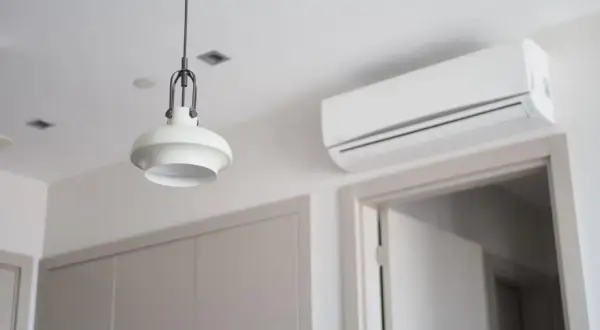Biała klimatyzacja ścienna nad drzwiami, obok lampy wiszącej.