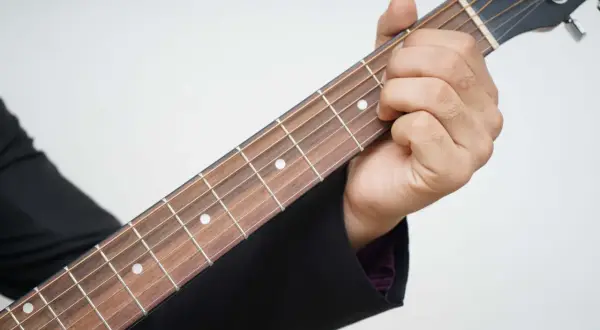 Dłoń dociska struny gitary, tworząc akord. Piękna muzyka na gitarę w zasięgu ręki.