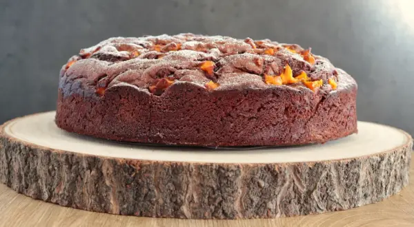 Torta al cioccolato con pezzi di mango, spolverata di zucchero a velo, su un tagliere di legno grezzo.