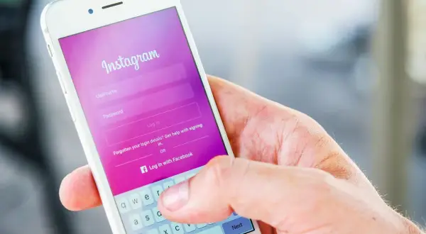 Dłoń trzyma smartfon z ekranem logowania Instagram. Widoczna opcja "Zapomniane dane logowania?" podpowiada, jak odzyskać hasło na Instagramie.