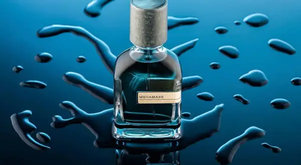 Szklana butelka perfum Megamare otoczona kroplami wody na granatowym tle.