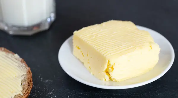 Frisch gemachte Butter auf einem Teller, daneben eine Scheibe Brot mit Butter bestrichen. So einfach kann Butter selber machen sein!