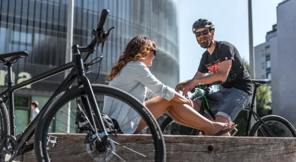 Ein Paar entspannt sich auf einer Holzbank mit Fahrrädern in einer modernen Stadt. Hier lebt es sich fahrradfreundlich.