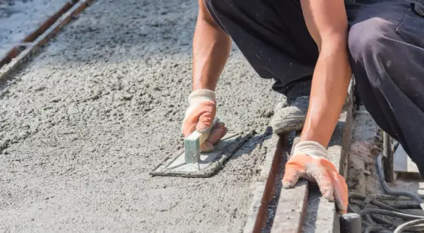 Robotnik wygładza świeży, mokry beton kielnią. Powierzchnia jest jeszcze wilgotna, ale wkrótce stanie się suchy beton.