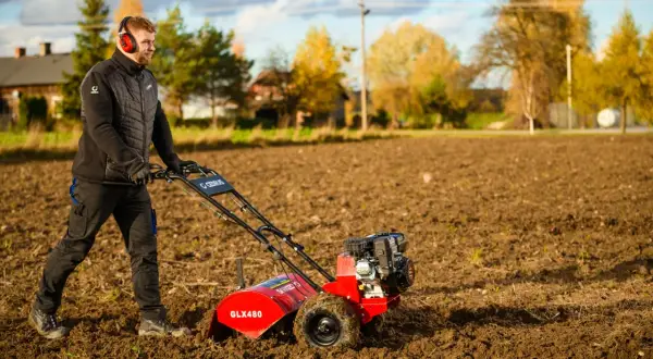 Mężczyzna w słuchawkach pracuje czerwoną glebogryzarką na polu.