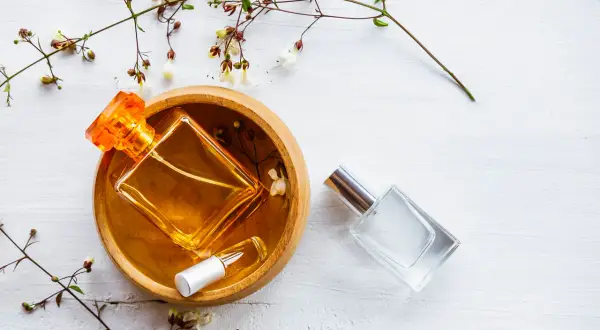 Dwie buteleczki perfum, jedna z bursztynowym płynem w drewnianej miseczce, druga szklana. Delikatne gałązki z kwiatami. Woda toaletowa ile alkoholu?