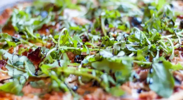 Pyszna pizza z tuńczykiem, rukolą i oliwkami, polana sosem balsamicznym.