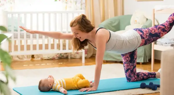 Mama wykonuje ćwiczenia po porodzie na macie, a jej maluch leży obok.