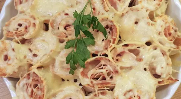Pyszna tortilla z szynką i serem na ciepło, zapieczona do złotego koloru, udekorowana gałązką natki pietruszki.