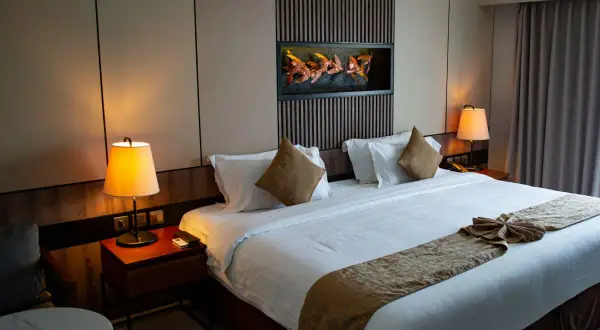 Przytulna sypialnia hotelowa z dużym łóżkiem, lampkami nocnymi i ozdobnym zagłówkiem.