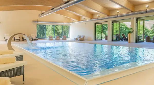 Entspannter Urlaub in Sachsen: Einladender Innenpool mit Wasserfall, Liegen und Blick ins Grüne. Perfekt für erholsame Tage.