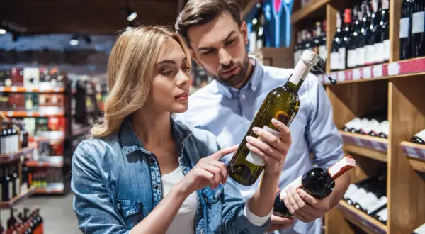 Para wybiera wino w sklepie. Kobieta wskazuje na etykietę, na której widnieje informacja, że produkt zawiera siarczyny.