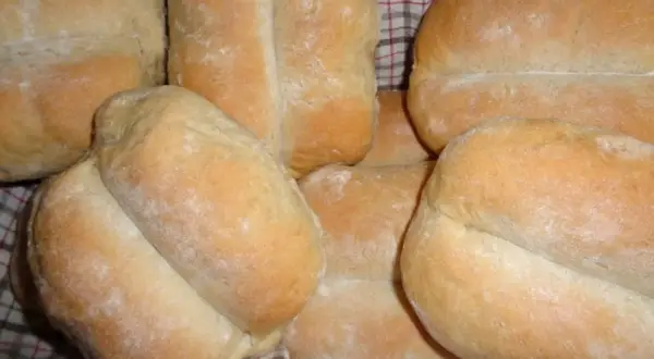 Świeżo upieczone bułki pszenno żytnie, lekko oprószone mąką, ułożone w koszyku.
