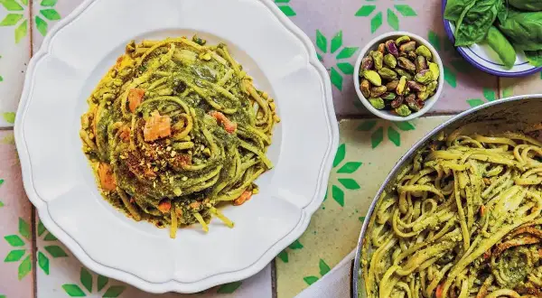 Makaron linguine z zielonym pesto, pistacjami i kawałkami łososia na białym talerzu.