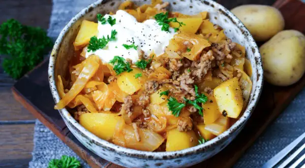 Herzhaftes Schichtkraut Rezept mit Hackfleisch, Kartoffeln und einem Klecks Sauerrahm, garniert mit Petersilie.