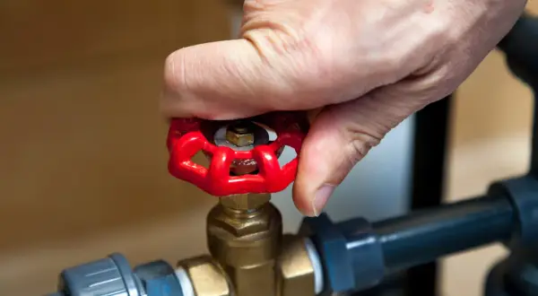 Dłoń obraca czerwony zawór grzybkowy, który jest częścią instalacji wodnej.