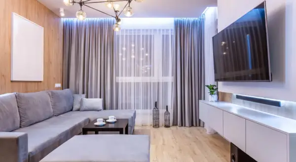 Nowoczesny salon w małym mieszkaniu 40 m: szara sofa, stolik kawowy, TV na ścianie i drewniana ściana.