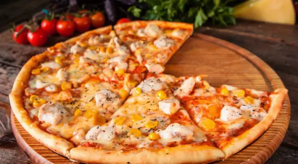 Pyszna pizza z kurczakiem i kukurydzą, podana na drewnianej desce, z pomidorkami koktajlowymi i bazylią w tle.