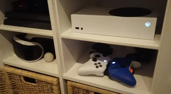 Biały Xbox Series S, który wyszedł w 2020 roku, stoi na półce obok konsoli PlayStation i kontrolerów.