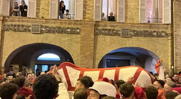Folla festante al carnevale di Offida, con un grande carro bianco e rosso che avanza tra la gente.