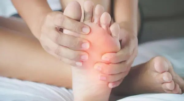 Mani che massaggiano la pianta del piede, evidenziando un'area arrossata che simboleggia il dolore.