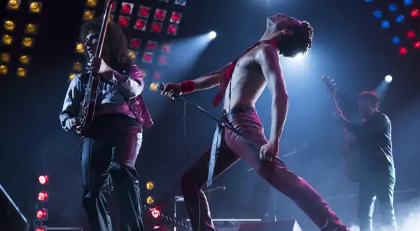 Freddie Mercury w czerwonym stroju, śpiewający na scenie, podczas gdy gitarzysta gra. To jest ich queen rhapsody.