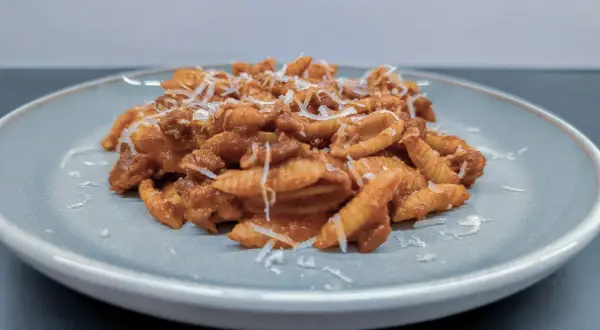 Gnocchi Sardi (Malloreddus) mit Tomatensoße und geriebenem Parmesan auf einem Teller.