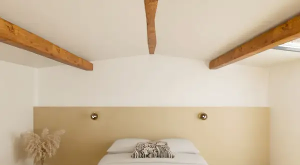 Chambre mansardée avec poutres apparentes. Quel mur peindre pour un effet cosy ? Le mur derrière le lit, avec sa tête de lit beige, semble idéal.